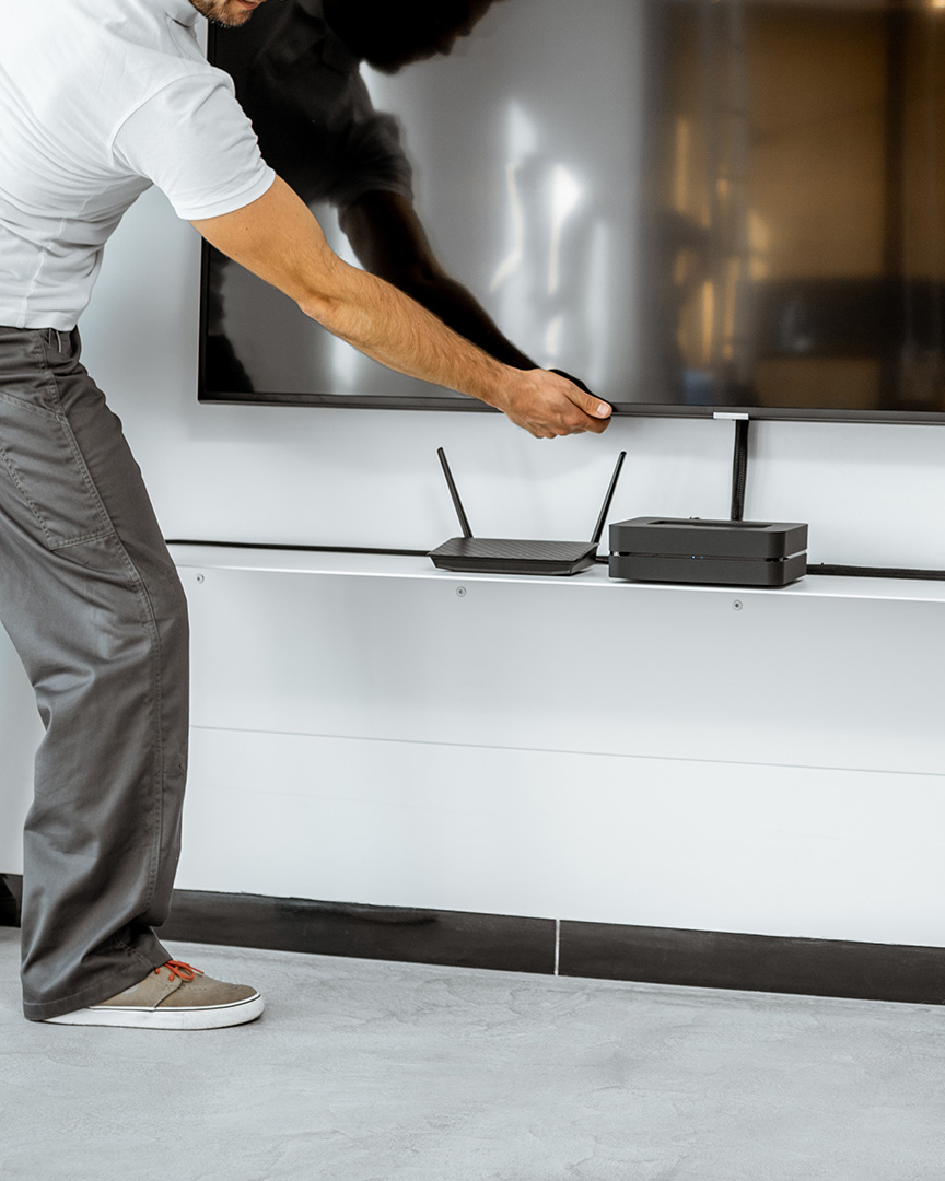 Two professional workmen in workwear installing a large TV monitor and audio system in the white living room. Home appliances installation concept